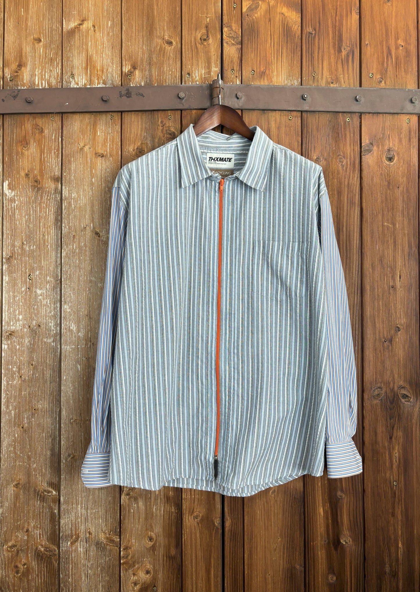 Ein hochwertiges hellblau-weiß gestreiftes Seersucker-Hemd mit einem orangefarbenen Reißverschluss anstelle einer Knopfleiste. Die Ärmel wurden ausgetauscht mit einem anderen gestreiften, hellblauen Hemd. Mit Kentkragen und Brusttasche.